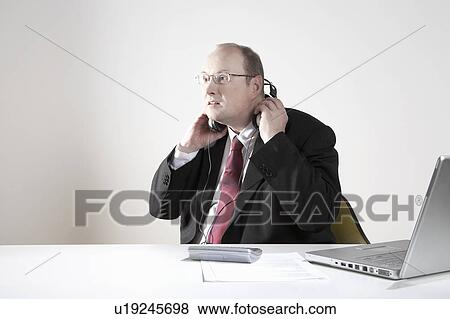 Stock Photo - Businessman with earphones at desk. Fotosearch