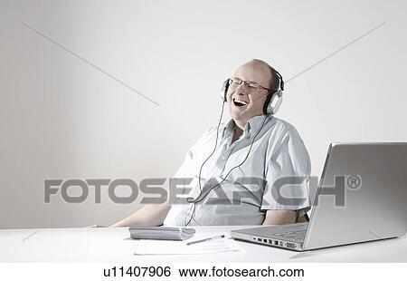 Businessman with earphones laughing at desk View Large Photo Image Stock Photograph - Businessman with earphones laughing at desk. Fotosearch