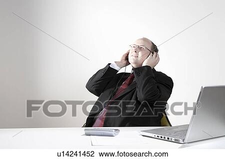 Businessman with earphones relaxing at desk View Large Photo Image Stock Image - Businessman with earphones relaxing at desk. Fotosearch