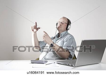 Stock Image - Businessman with earphones relaxing at desk. Fotosearch