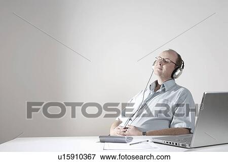 Stock Photo - Businessman with earphones relaxing at desk. Fotosearch