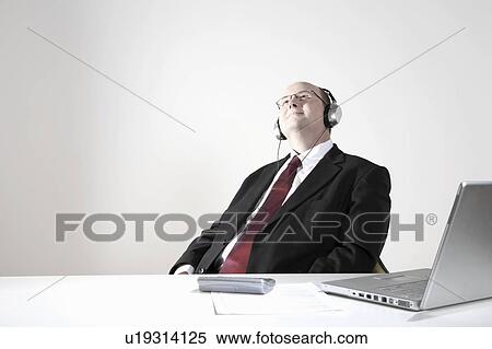 Businessman with earphones relaxing at desk View Large Photo Image Stock Photography - Businessman with earphones relaxing at desk. Fotosearch