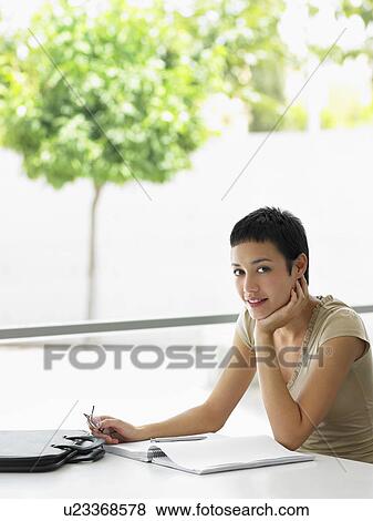 Businesswoman sitting at office desk with files, portrait View Large Photo Image Stock Photo - Businesswoman sitting at office desk with files, portrait. Fotosearch