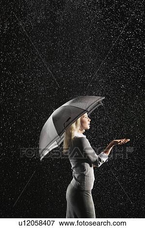 Stock Photo - Businesswoman sticking hand out from under umbrella during rain, side view. Fotosearch