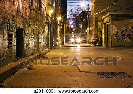 Stock Image - Car head lights in alleyway at dusk. Fotosearch