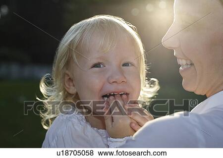 Stock Photo - Close-up of mother embracing daughter (3-4) with fingers in mouth. Fotosearch