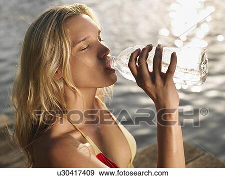Stock Photo - Close-up of young woman in bikini drinking from bottle on jetty. Fotosearch