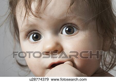Stock Photo - Close-up portrait of child (6-12 months) with finger in mouth. Fotosearch