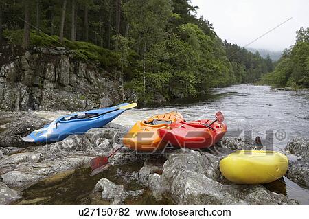 Stock Image - Colourful kayaks by river. Fotosearch