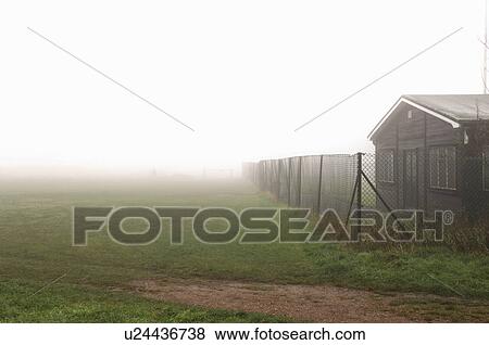 Stock Photo - Cottage behind chainlink fence on foggy day. Fotosearch