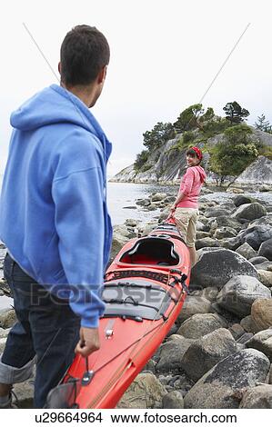 Picture - Couple carrying kayak to ocean. Fotosearch