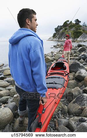 Stock Photo - Couple carrying kayak to ocean. Fotosearch