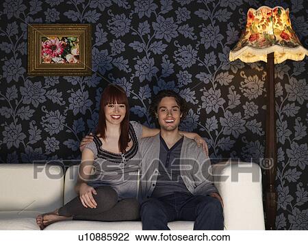 Stock Image - Couple embracing sitting on sofa, portrait. Fotosearch
