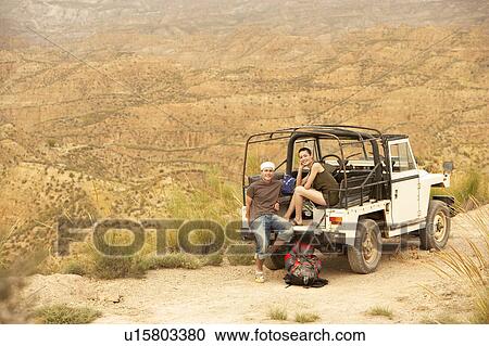 Couple sitting at back of four wheel drive car on edge of cliff in desert View Large Photo Image Stock Image - Couple sitting at back of four wheel drive car on edge of cliff in desert. Fotosearch