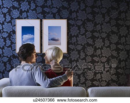 Stock Photograph - Couple sitting on sofa looking at each other, back view. Fotosearch
