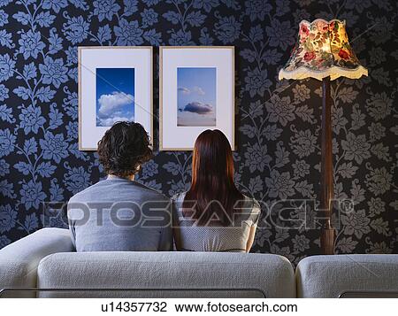 Couple sitting on sofa looking at pictures on wall, back view View Large Photo Image Stock Image - Couple sitting on sofa looking at pictures on wall, back view. Fotosearch