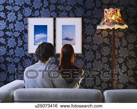 Couple sitting on sofa looking at pictures on wall, back view View Large Photo Image Stock Photograph - Couple sitting on sofa looking at pictures on wall, back view. Fotosearch