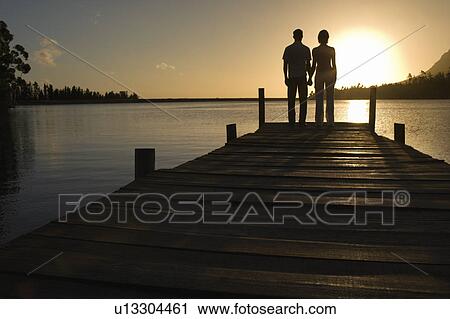 Couple standing on dock by lake, holding hands, back view. View Large Photo Image Stock Image - Couple standing on dock by lake, holding hands, back view.. Fotosearch