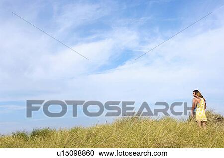 Stock Image - Couple Standing on grassy dune looking out to sea. Fotosearch