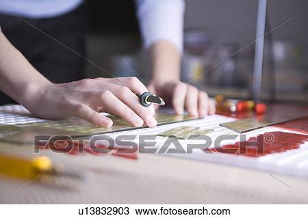 Stock Image - Craftswoman cuts glass with precision scalpel. Fotosearch
