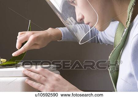 Stock Image - Craftswoman works with glass on bench wearing visor. Fotosearch