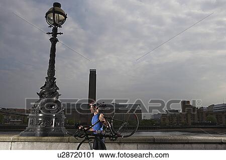 Cyclist carrying bicycle along river embankment, side view, London, England View Large Photo Image Stock Image - Cyclist carrying bicycle along river embankment, side view, London, England. Fotosearch