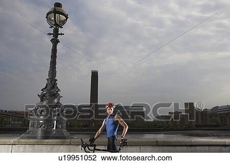 Stock Image - Cyclist on bicycle standing by river embankment, London, England. Fotosearch