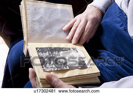 Stock Image - Elderly lady sits looking at photograph album. Fotosearch