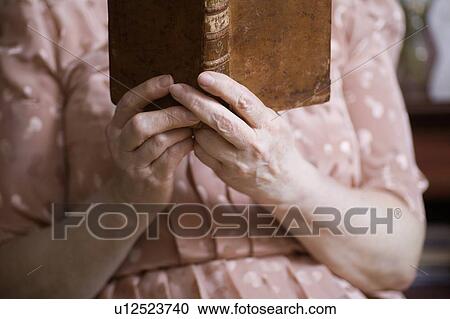 Stock Image - Elderly woman sits reading book. Fotosearch