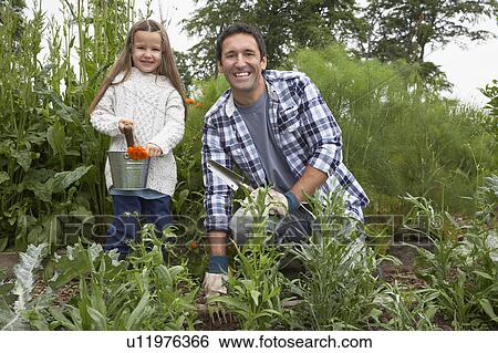 Stock Photograph - Father and daughter (5-6) gardening, portrait. Fotosearch