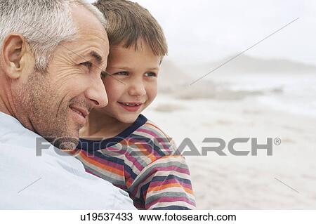 Stock Image - Father and son (5-6) on beach, close-up. Fotosearch