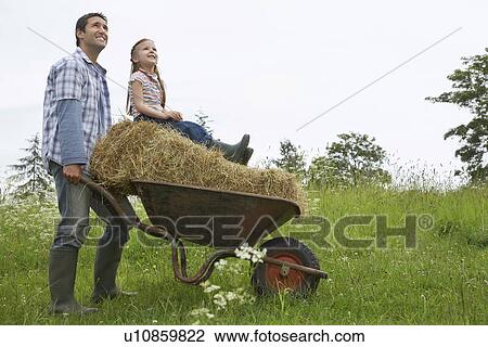 Father pushing daughter (5-6) on wheelbarrow in field View Large Photo Image Stock Image - Father pushing daughter (5-6) on wheelbarrow in field. Fotosearch