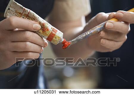 Stock Image - Female painter squeezing red paint on brush. Fotosearch