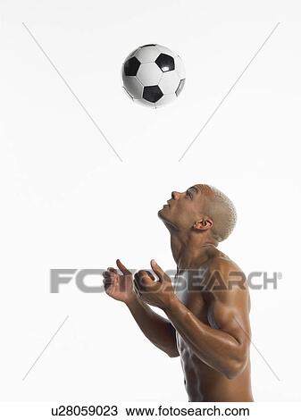 Stock Image - Football player looking up at ball in mid-air, side view. Fotosearch