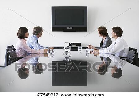 Stock Image - Four business colleagues watching flat screen television in conference room. Fotosearch