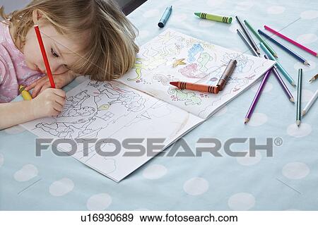 Stock Photo - Girl (3-4) resting head on arm, colouring in book, elevated view. Fotosearch