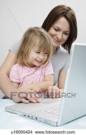 Picture - Girl (3-4) sitting on mother's lap, looking at laptop, smiling. Fotosearch