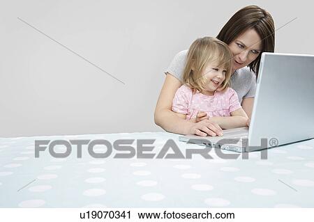 Girl (3-4) sitting on mother's lap, looking at laptop, smiling View Large Photo Image Stock Image - Girl (3-4) sitting on mother's lap, looking at laptop, smiling. Fotosearch