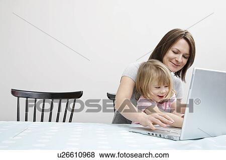 Girl (3-4) sitting on mother's lap, playing with laptop View Large Photo Image Stock Photo - Girl (3-4) sitting on mother's lap, playing with laptop. Fotosearch