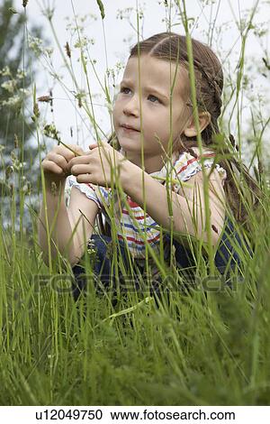 Stock Image - Girl (5-6) crouching in meadow. Fotosearch