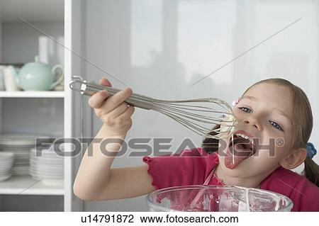 Stock Image - Girl (5-6) licking cream from wire whisk. Fotosearch