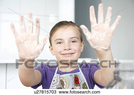 Stock Image - Girl (5-6) showing hands covered in flour, portrait. Fotosearch