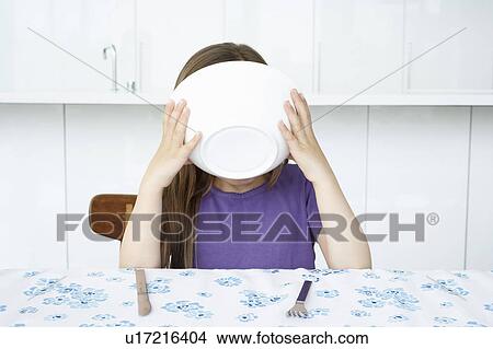 Picture - Girl (5-6) sitting at table, drinking from bowl. Fotosearch