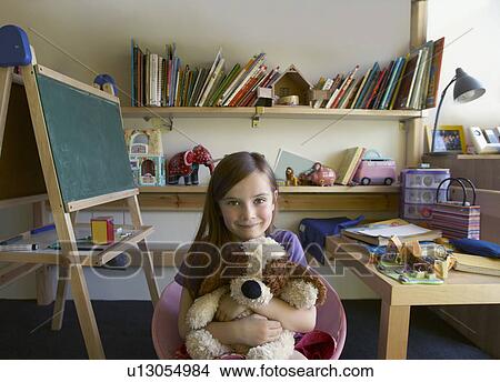 Picture - Girl (5-6) sitting in room, hugging soft toy. Fotosearch