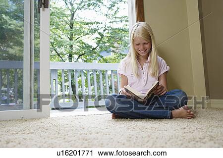 Stock Image - Girl (7-9) sitting cross-legged reading book, smiling. Fotosearch
