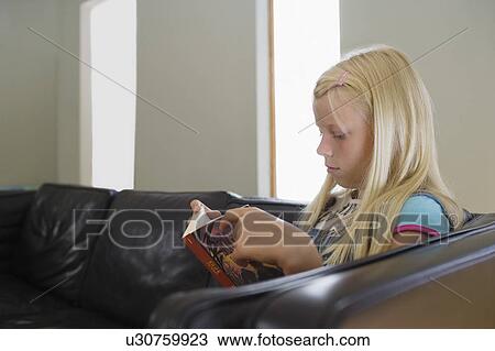Girl (7-9) sitting on sofa reading book View Large Photo Image Stock Image - Girl (7-9) sitting on sofa reading book. Fotosearch