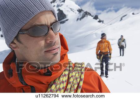 Picture - Hiker joined by safety line to two friends behind in snowy mountains. Fotosearch