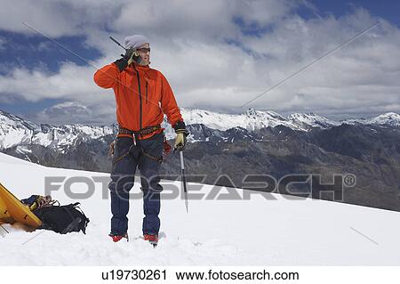 Stock Image - Hiker using walkie-talkie on snowy mountain peak. Fotosearch