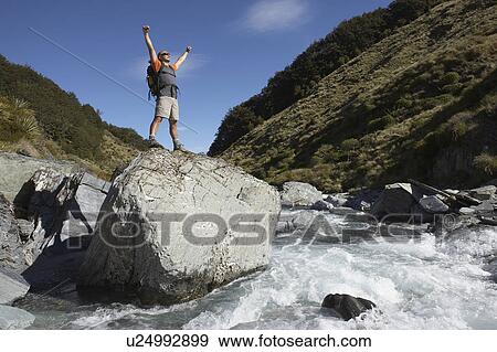 Stock Photo - Hiker with arms outstretched on rock in river. Fotosearch