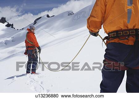 Stock Image - Hikers joined by safety line in snowy mountains. Fotosearch